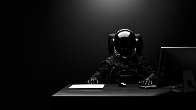 An Astronaut in a black spacesuit sitting at a desk
